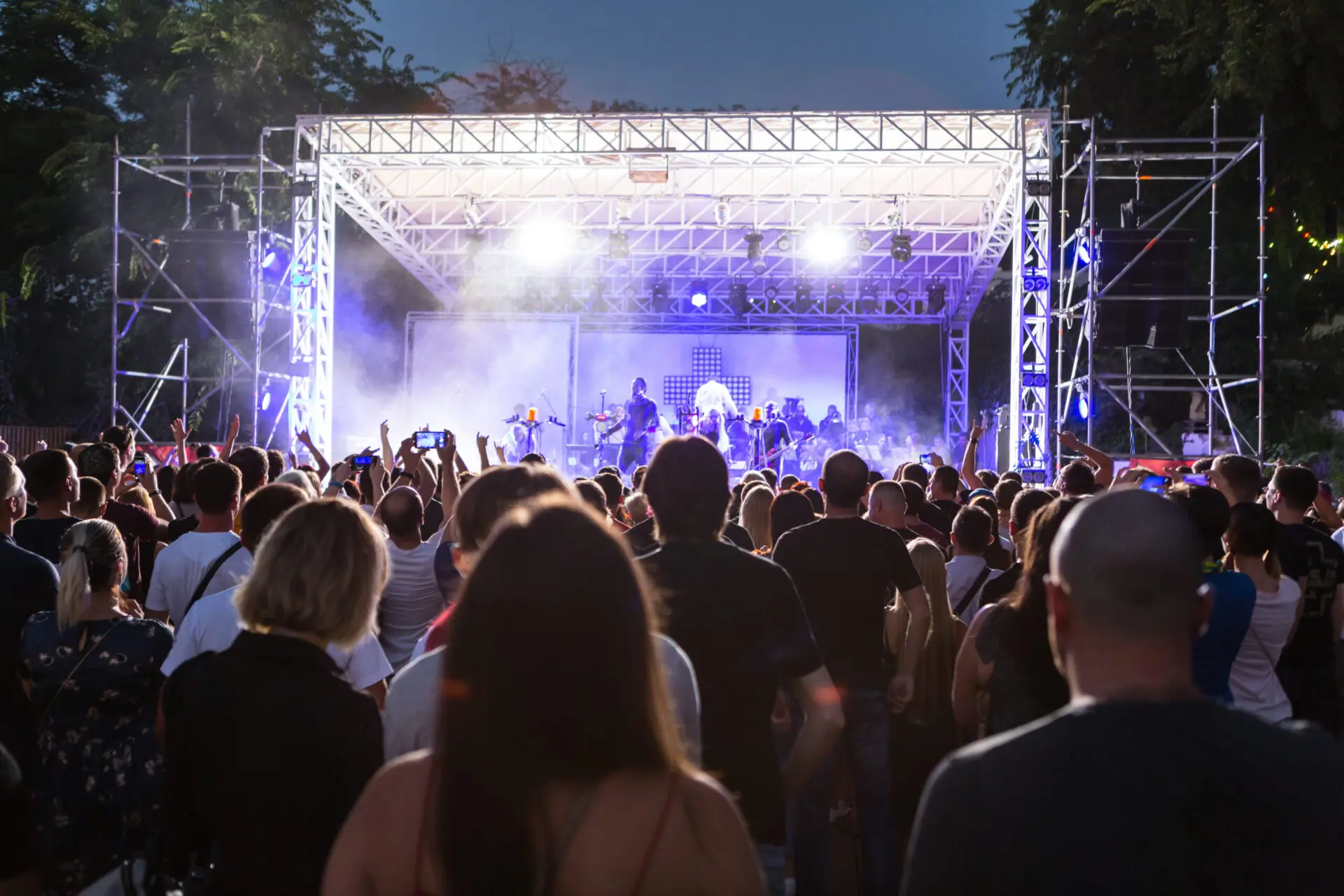 Rear view of crowd with arms outstretched at concert. cheering crowd at rock concert. silhouettes of concert crowd in front of bright stage lights. Crowd at music concert, audience raising hands up